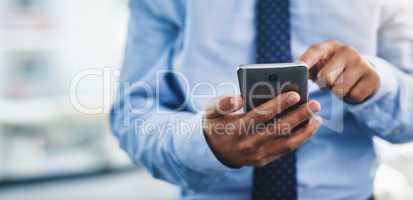 Taking a quick look at my social media. Cropped shot of an unrecognizable businessman standing alone in the office and using his cellphone to text.