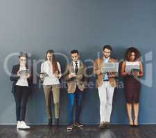 Waiting it out in the name of success. Studio shot of a group of businesspeople using wireless technology while waiting in line against a gray background.