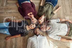 We keep it casual but always professional. High angle portrait of a group of colleagues lying together in a circle on the floor at work.