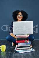 Knowledge is the greatest tool. Studio shot of a young woman using a laptop with books stacked in front of her against a blue background.