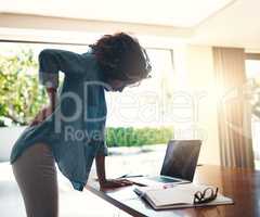 Wow, that hurts a lot. Shot of a young woman holding her back in pain while getting up from her desk at home.