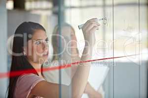 Charting the expected results. A young businesswoman writing down plans on a glass pane.