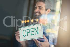 Time to serve some awesome coffee. Shot of a handsome young man hanging up an open sign on the door of his store.