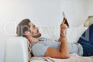 Catching up on my favorite weekly shows. Shot of a young man browsing the internet at home on a digital tablet.