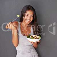 A bowl of my best salad ingredients. Portrait of a healthy young woman eating a salad against a gray background.