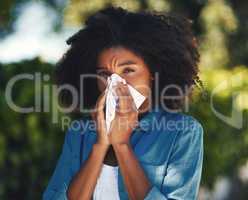 Its allergy season.... Portrait of a young woman blowing her nose with a tissue outside.