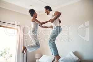 Theres so much fun in this relationship. Full length shot of an affectionate young couple jumping playfully on their bed at home.