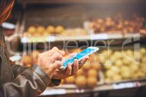 Status update Doing the weekly grocery run. Cropped shot of a woman using a mobile phone in a grocery store.