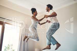 Taking each other to newer heights. Full length shot of an affectionate young couple jumping playfully on their bed at home.