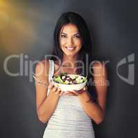 Its a bowl full of goodness. Portrait of a healthy young woman eating a salad against a gray background.