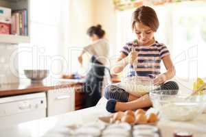 Shes a great little helper in the kitchen. Shot of a little girl helping her mom bake in the kitchen.
