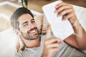 Comfortably connected. Shot of a young man using wireless technology on the sofa at home.