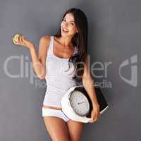 Snacking that helps the scale give good news. Shot of a beautiful and healthy young woman holding an apple and a scale.