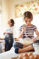 Shes messy but a natural. Shot of a little girl helping her mom bake in the kitchen.