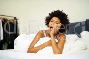 Five.More.Minutes. Shot of a tired young woman yawning in bed at home.