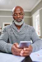 Now you can bank from anywhere. Cropped shot of a senior man using his cellphone while working on his finances at home.