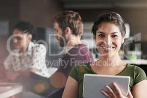 Getting easy access to information in a growing business. Portrait of a young woman using a digital tablet in a modern office with her colleagues in the background.