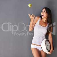 Happy snacking. Shot of a healthy young woman throwing an apple into the air while holding a scale.