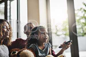 Every family has their favourite tv show. Shot of a happy young family of three watching tv from the sofa at home.