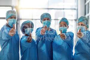 The surgery was a success. Portrait of a group of medical practitioners showing thumbs up in a hospital.