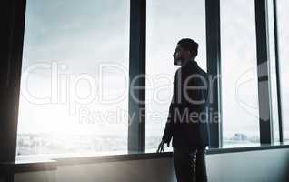 On a whole new level. Shot of a young businessman looking thoughtfully out of an office window.