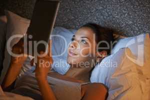 Bedtime bliss. Beautiful young woman playing on her digital tablet before bed.