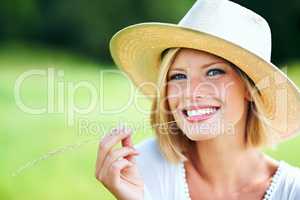 Countryside cutie. Cute young woman smiling while wearing a hat and chewing a wheat stalk.