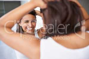 Getting ready is half the funof going out. A cropped shot of a happy young woman deciding on a hair style in front of her bathroom mirror.