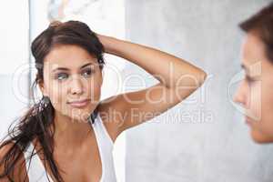 Deciding on a style for tonight. A cropped shot of a beautiful young woman deciding on a hair style in front of her bathroom mirror.