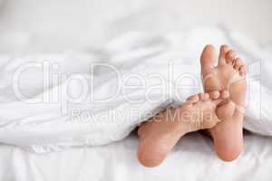 Wiggling toes of wakefulness. Shot of a pair of womans feet poking out from under the sheets of a bed.