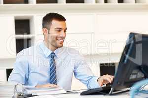 Ive got new client emails. A positive young businessman working at his desk in front of his computer.