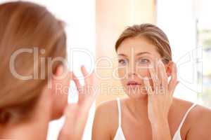Taking care of her skin. A naturally gorgeous woman applying moisturizing cream in a mirror.
