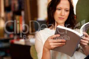 Immersed in the words. A young woman quietly reading a book while seated in a chair.