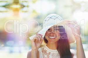 Protecting my skin against the summer sun. A happy young woman standing in the park wearing a sunhat.