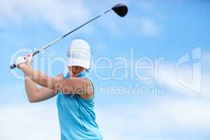 The trick is to keep your head down. A young female golfer swinging a golf club (driver) over her head about to take a shot - copyspace.