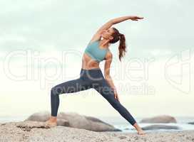 Feel the positive energy flow through your body. Shot of a sporty young woman practicing yoga at the beach.