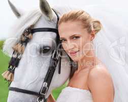 Her most trusted steed will spirit her to the aisle. Portrait of a gorgeous blonde bride standing alongside her stallion.