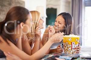 We havent done this in ages. Shot of three attractive young women eating popcorn on their girls night.