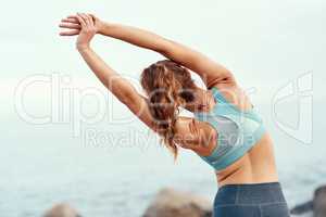 Feel the flow of the day. Rearview shot of a sporty young woman stretching her arms while exercising outdoors.