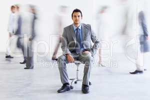 Keeping calm during the rush. Conceptual portrait of a young executive sitting as colleagues stream passed him hastily.