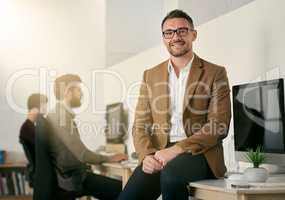 The expert in anything was once a beginner. Shot of a designer sitting on a desk with his colleagues blurred in the background.