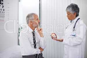 Three tablets, twice a day. A mature doctor giving a bottle of pills to one of her patients during a checkup.