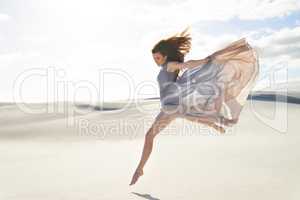 Freedom and isolation on the beach. Side view of a beautiful young woman in a flowing dress jumping across sand.