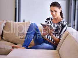 Leisurely browsing. A beautiful young woman using a tablet on her couch.