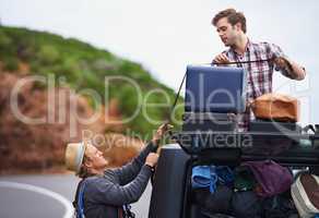 Think we brought too much. Shot of two young men stopped at the side of the road and repacking their truck.