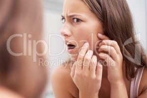 What A pimple. A young woman looking shocked as she examines her skin.