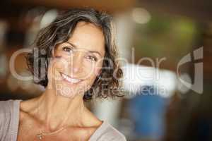 Laughter kept her heart young. A mature woman smiling happily while standing indoors at home.