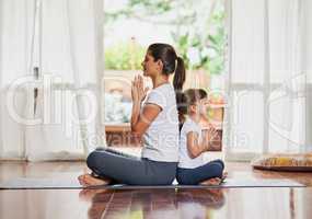 Some peace and harmony with my child. Shot of a focused young mother and daughter doing a yoga pose together while being seated against each others back.