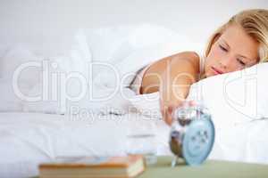 Just another five minutes.... Young woman sleeping in with her alarm clock next to her.