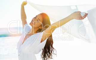 Lost in the sensation of freedom. Beautiful young woman holding up a linen cloth as the wind catches it.